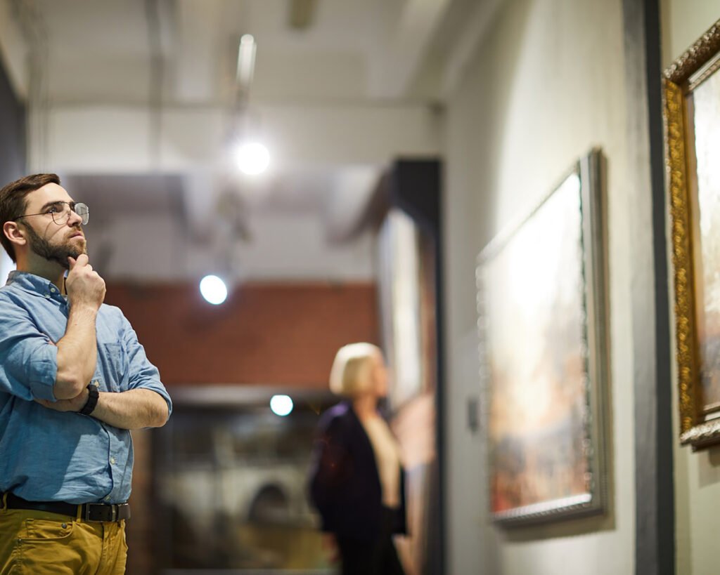 Portrait of pensive bearded man looking at paintings standing in art gallery or museum, copy space